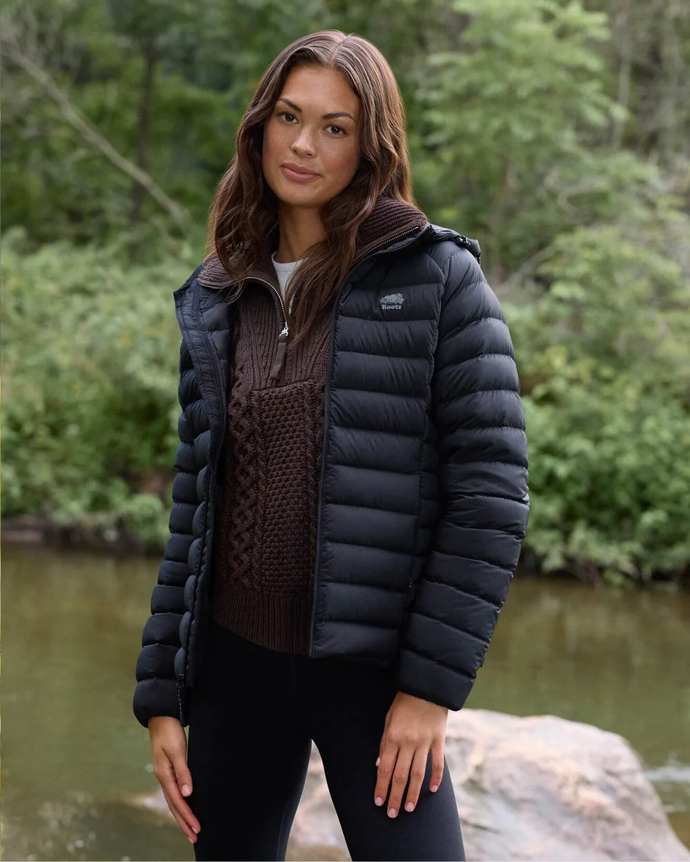 Woman in a black puffer jacket by a wooded lake