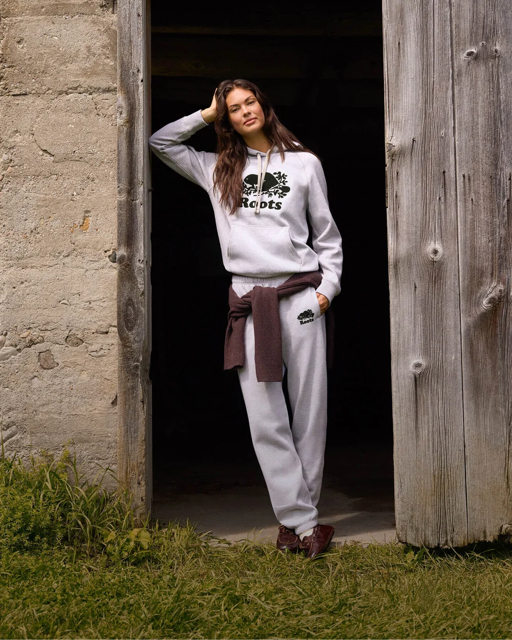 Woman in a matching grey sweatshirt and sweatpants by a rustic doorway